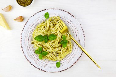 Pesto soslu spagetti makarna ve beyaz ahşap arka planda bir tabakta fesleğen. Üst görünüm.