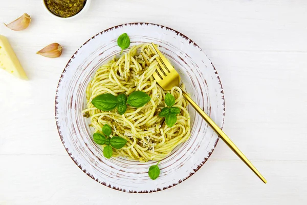 Pesto soslu spagetti makarna ve beyaz ahşap arka planda bir tabakta fesleğen. Üst görünüm.
