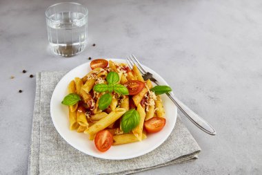 Beyaz tabakta, gri arka planda domatesli makarna ve fesleğen. Kopyalama alanı olan üst görünüm. Yüksek kalite fotoğraf