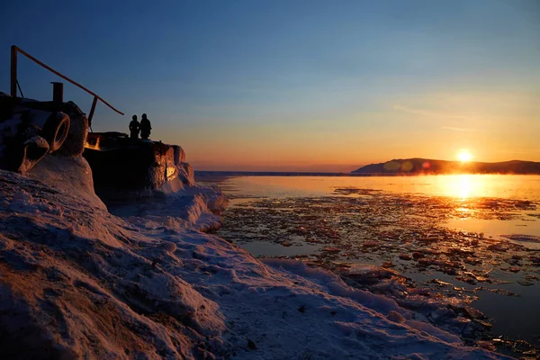 Beau coucher de soleil sur le lac Baïkal. Sur la jetée, un homme et une femme regardent le coucher du soleil. La fonte de la glace dans le lac. — Photo