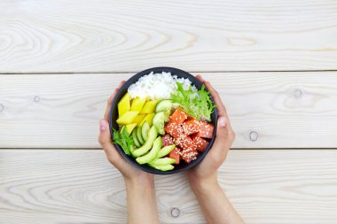 Bir kase somon, pirinç, avokado, salatalık, mango, bir kadının ellerinde otlar. Hawaii ahi 'si, balıklı diyet yemeği. Üst görünüm. 