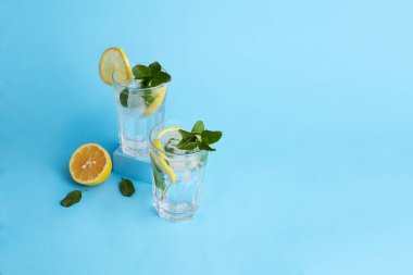 Soğuk, ferahlatıcı bir yaz içeceği. İki bardak limonata ya da limonlu mojito kokteyli ve mavi arka planda nane. Yaratıcı kavram