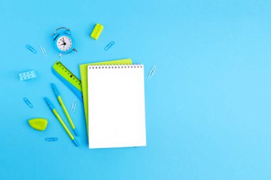 School supplies. Empty notebook, pens, ruler, alarm clock, paper clips, rubber band. Green and blue colors.
