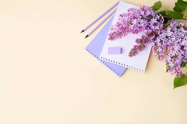 A notebook, pencils, and lilac branches on a yellow background. The concept of home comfortable learning.