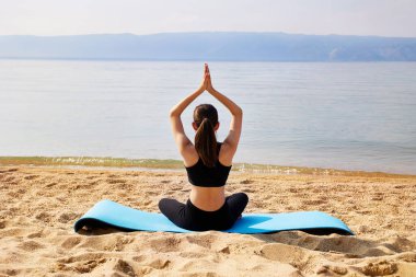 Genç bir kız kumlu bir sahilde yoga yapıyor. Meditasyon ve dinlenme. Doğayla birlik.