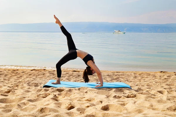 Sportif bir kız kumlu bir plajda egzersiz yapıyor. Yoga ya da fitness zamanı. Doğayla birlik.