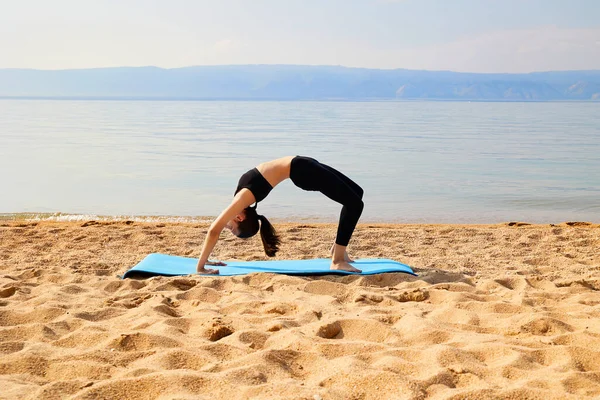 İnce bir kız gölün kıyısındaki kumlu bir sahilde egzersiz yapıyor. Yoga ya da fitness zamanı. Doğayla birlik. 