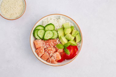 Somon, pirinç, avokado, salatalık, biber ve susam tohumlarıyla dolu bir kase. Balıklı geleneksel Hawai yemeği. Üst görünüm.