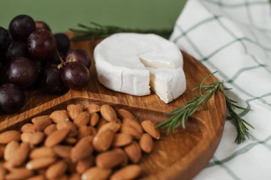 Camembert peyniri, fındık ve üzüm. Yeşil arka planda lezzetli ve sağlıklı bir yemek. Ahşap tabaklarda yararlı ve sağlıklı yiyecekler..