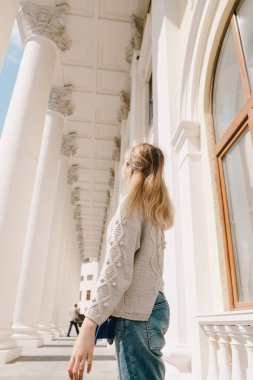 Büyük beyaz kolonların arka planında örülü süveter ve kot pantolon giyen bir kız. Yaşam biçimi