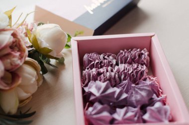 Masanın üzerindeki kutuda pembe pasta ve çiçekler var. Yiyecek.