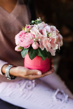 Elinde pembe bir kutuda suni dekoratif çiçekler tutan bir kız. çiçek aranjmanı