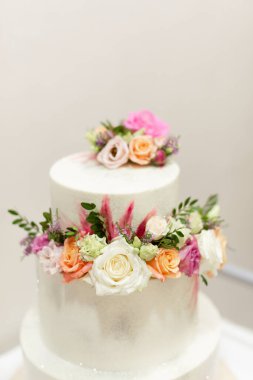 Beyaz arka planda çiçeklerle süslenmiş beyaz bir düğün pastası. Düğün pastası.