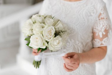 Beyaz elbiseli gelin elinde bir gelin buketi tutuyor. Düğün detayları