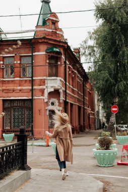 Ceketli sarışın kız arka taraftan sokak manzarasına doğru koşuyor. Şehir yürüyüşü