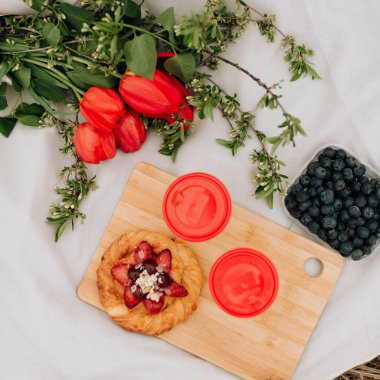Beyaz ekose üzerinde tatlı çörekler ve çiçekler, çimlerin üzerinde yaz pikniği. Yaz