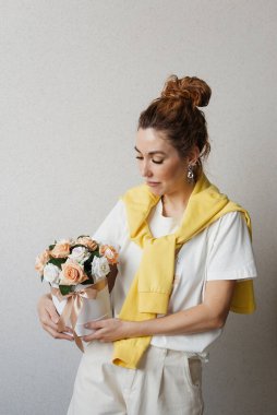 Parlak ceketli bir kadın bir buket çiçeği bir kutuda tutuyor.