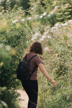 Sırtında sırt çantası olan kıvırcık saçlı kız yazın parkta yürüyor.