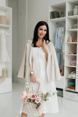 stylish brunette in a white dress and jacket with a basket of flowers in the studio