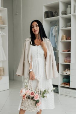 stylish brunette in a white dress and jacket with a basket of flowers in the studio