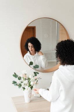 Beyaz kazaklı, Afrikalı bukleli esmer bir kadın eliyle bir buket çiçeğe dokunuyor.