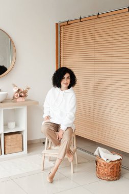 Beyaz kazaklı Afrikalı kadın tahta sandalyede oturuyor.