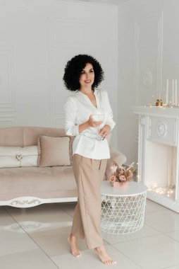 Kıvırcık saçlı kadın, pembe kanepe ve şöminenin arka planında parmak uçlarında duruyor.