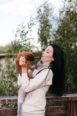 Esmer kız kucağında küçük kahverengi bir köpek tutuyor.