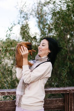Gülümseyen esmer kız kucağında küçük kahverengi bir köpek tutuyor.