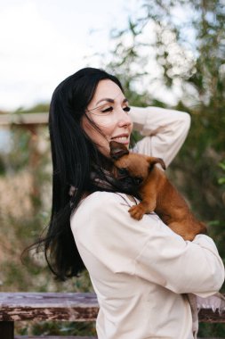 Açık renk elbiseli genç bir kız küçük köpeğini kollarında tutuyor.