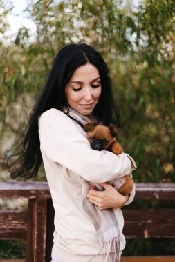 Açık renk elbiseli genç bir kız küçük köpeğini kollarında tutuyor.