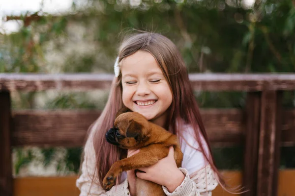 little girl laughs and holds a small brown dog in her arms