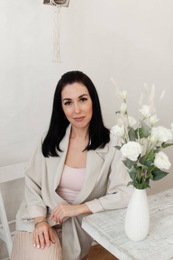 Açık renk ceketli güzel esmer kız masada oturuyor.