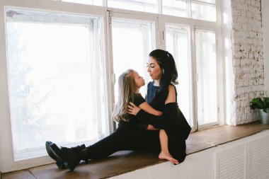 Çok şık bir anne ve kız çıplak ayakla pencere eşiğinde sarılıyorlar.