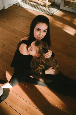 Güzel esmer anne ve uzun saçlı kızı yerde oturuyorlar.