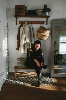 Siyah elbiseli şık esmer kız ayakkabılarını koridora bağlıyor.