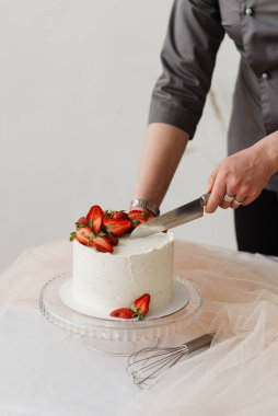 Pasta şefi, beyaz çilekli pastayı bıçakla keser.