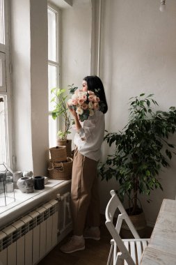 Şık esmer kız elinde bir buket çiçekle dikiliyor.