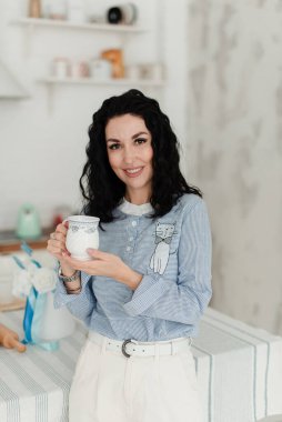 Mavi gömlekli, elinde beyaz bir kupayla güzel bir esmer kız.