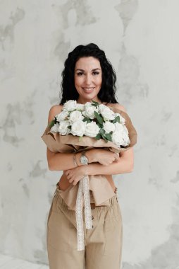 Güzel esmer model göğsüne büyük bir buket çiçek bastırıyor.