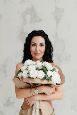 Güzel esmer model, çıplak göğüslerini büyük bir buket çiçekle kaplıyor.