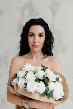 Güzel esmer model, çıplak göğüslerini büyük bir buket çiçekle kaplıyor.