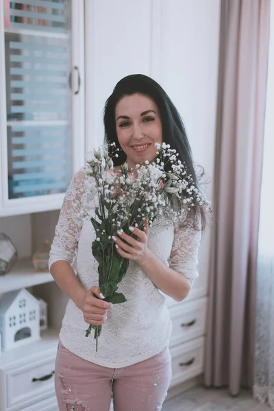 a sweet brunette girl in a white t-shirt holds a bouquet of fresh flowers at home