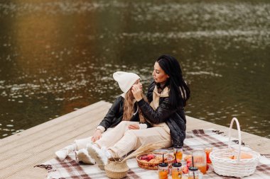 Parkta göl kenarında piknik yapan deri ceketli şık bir anne ve kız.