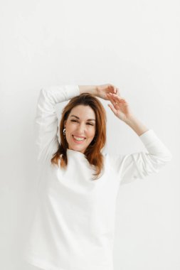 Beyaz kazaklı güzel kız ellerini başının üstünde tutuyor.