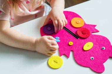 Montessori oyuncağını ilikleyen küçük kız. Pratik yaşam becerileri, kişisel bakım, erken eğitim, aktiviteler ve çocuk parmaklarının becerisini geliştirmek için oyuncak, pratik yaşam, öğrenme renkleri.  