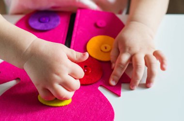 Montessori oyuncağını ilikleyen küçük kız. Pratik yaşam becerileri, kişisel bakım, erken eğitim, aktiviteler ve çocuk parmaklarının becerisini geliştirmek için oyuncak, pratik yaşam, öğrenme renkleri.  