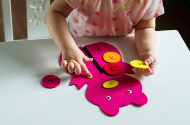 Montessori oyuncağını ilikleyen küçük kız. Pratik yaşam becerileri, kişisel bakım, erken eğitim, aktiviteler ve çocuk parmaklarının becerisini geliştirmek için oyuncak, pratik yaşam, öğrenme renkleri.  