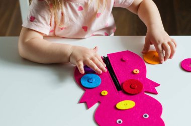 Montessori oyuncağını ilikleyen küçük kız. Pratik yaşam becerileri, kişisel bakım, erken eğitim, aktiviteler ve çocuk parmaklarının becerisini geliştirmek için oyuncak, pratik yaşam, öğrenme renkleri.  