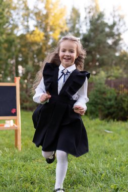 Okul üniformasıyla dışarıda oynayan neşeli beyaz kadın çocuk bilginin, çocukluk eğitiminin ve okul hayatının beklentisinin sembolü.